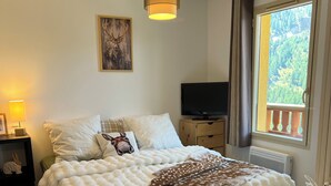 A cozy bedroom with a bed, a TV, a window with a view, and a lamp.
