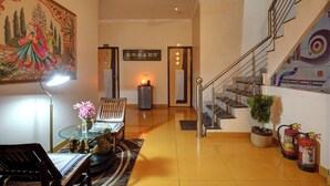 A spacious lobby with a staircase, a large decorative painting, a table with flowers, and a fire extinguisher. - Shyama inn by Rivlet  (New Delhi)