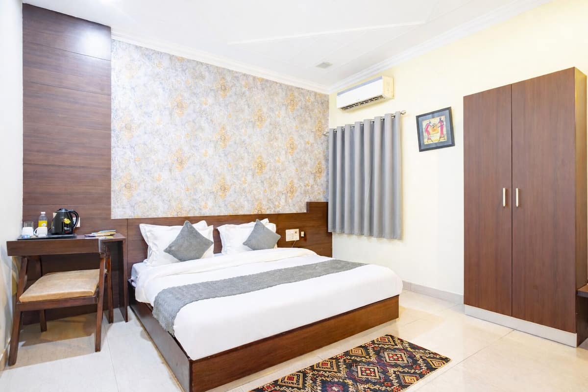 A hotel room with a bed, a desk, a wardrobe, and a patterned wall.