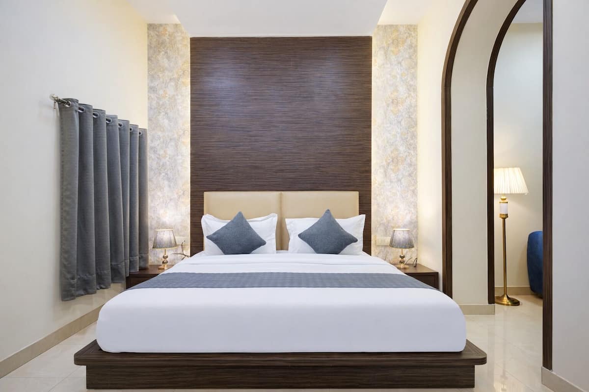 A modern hotel room with a large bed, two bedside tables with lamps, a mirror, and a view of the hallway.