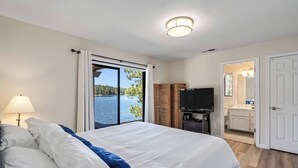 Habitación de hotel con una cama grande, televisor, baño y vista a un lago.