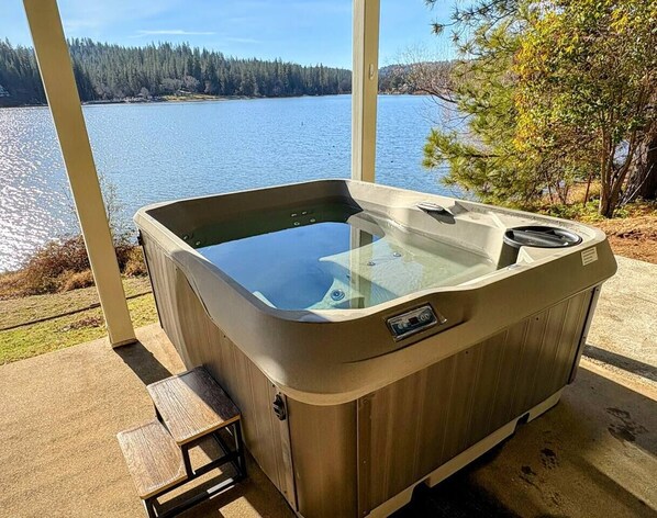 A hot tub with a glass top, positioned on a concrete deck with a view of a lake and trees.
