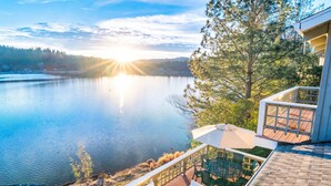 Terraza con mobiliario exterior que da a un lago, un bote amarrado en la orilla y vistas del bosque circundante.
