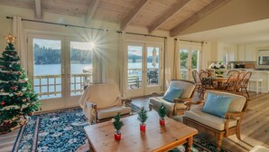 Un salón acogedor con un gran ventanal con vistas a un lago, muebles de madera y un árbol de Navidad.