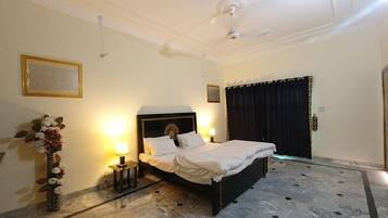 A hotel room with a bed, a nightstand, a lamp, a vase of flowers, and a door with a curtain.