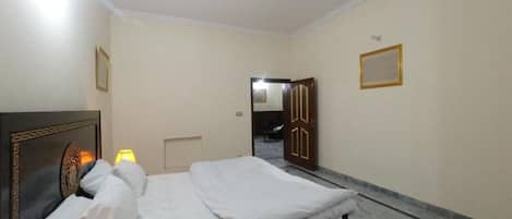 A hotel room with a bed, a nightstand, a lamp, and a door leading to another room.