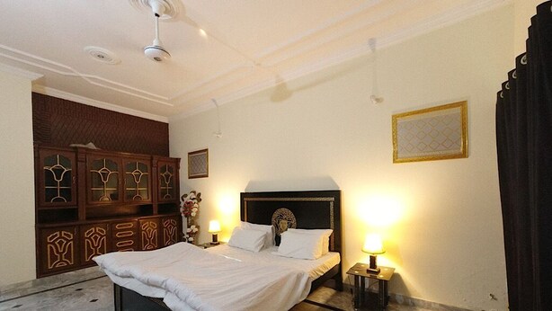 A hotel room with a bed, a nightstand with a lamp, a decorative cabinet, and a ceiling fan. - Room-room in Asga Best Hostel Versace ho (Rawalpindi)