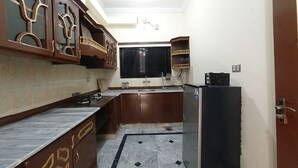 A compact kitchen with dark wooden cabinets, a marble countertop, and a black refrigerator. - Room-room in Asga Best Hostel Versace ho (Rawalpindi)