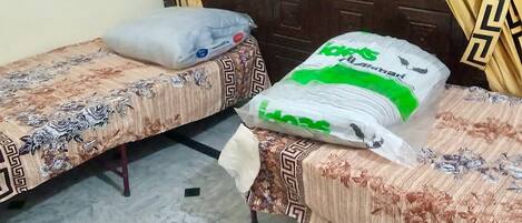 Two single beds with floral-patterned bedspreads, a large white bag with green text, and a window with curtains.