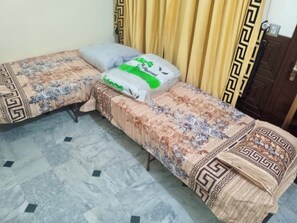 Two single beds with patterned bedding, a marble floor, and a wooden door.