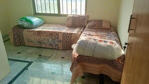 Een kamer met twee bedden, elk voorzien van beddengoed en kussens met een patroon, een raam met tralies en een betegelde vloer.