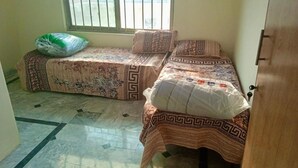 Een kamer met twee bedden, elk voorzien van beddengoed en kussens met een patroon, een raam met tralies en een betegelde vloer.