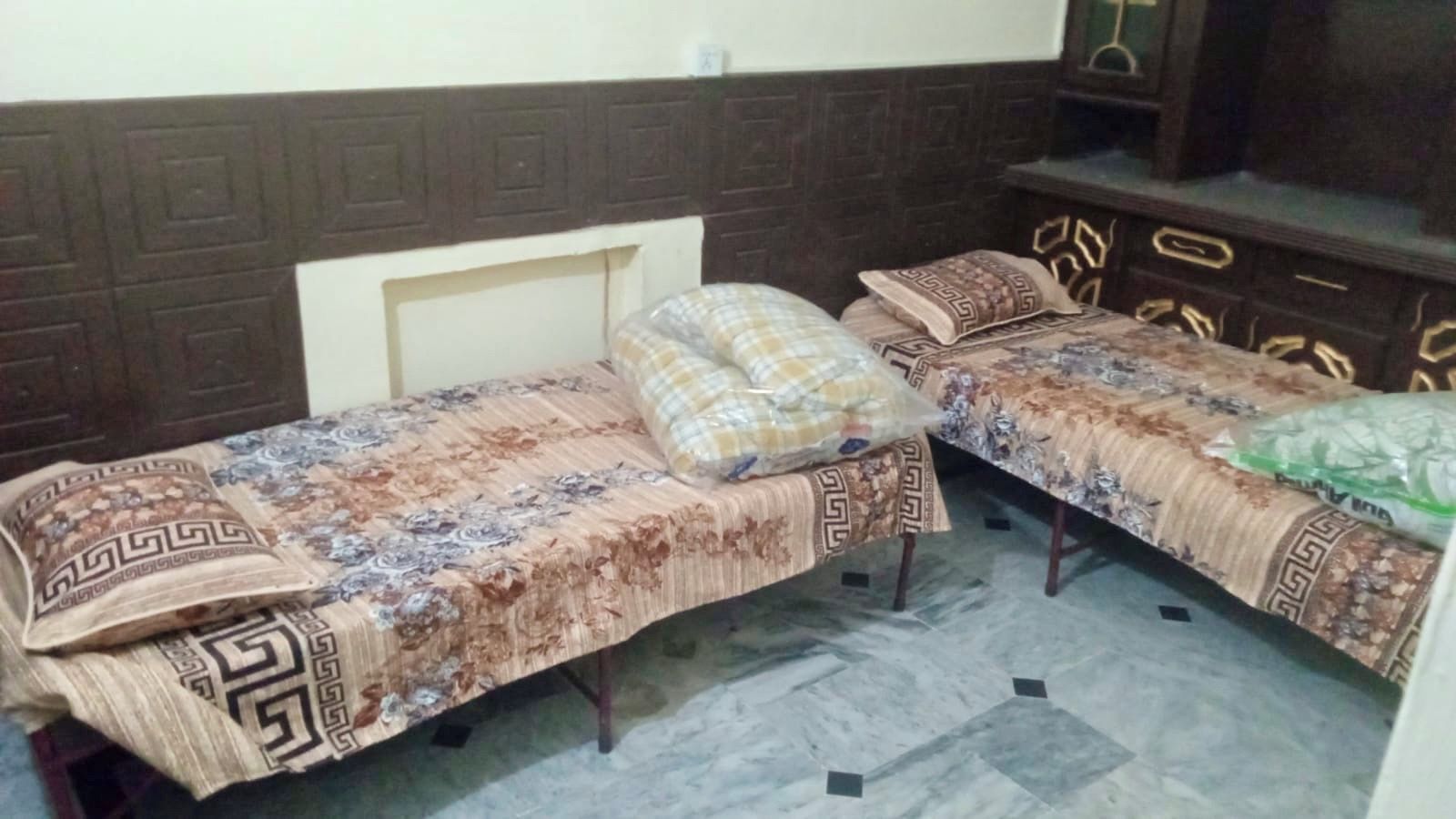 Two single beds with patterned bedspreads and matching pillows, a wooden headboard, and a tiled floor.