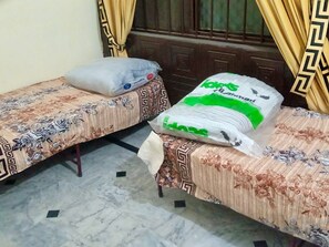 Two single beds with floral-patterned bedspreads, a large white bag with green text, and a window with curtains. - Room-room Serene Retreat in Rawalpindi - (Rawalpindi)