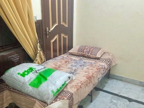 A single bed with a patterned bedspread and a green pillow, a wooden door, and a curtain. - Room-room Serene Retreat in Rawalpindi - (Rawalpindi)
