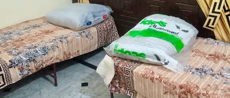 Dos camas individuales con ropa de cama de estampado floral, un gran saco de detergente para la ropa y una ventana con cortinas.