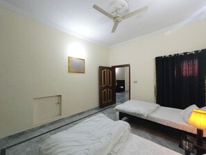 A hotel room with two single beds, a ceiling fan, a mirror, a door, and a curtain. - Room-serene Retreat in Rawalpindi - Your (Rawalpindi)