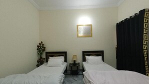 A hotel room with two single beds, a nightstand with a lamp, a framed picture on the wall, and a curtain with a geometric pattern. - Room-serene Retreat in Rawalpindi - Your (Rawalpindi)