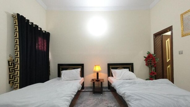 A hotel room with two single beds, a nightstand with a lamp, a marble floor, and a door with a decorative frame. - Room-serene Retreat in Rawalpindi - Your (Rawalpindi)