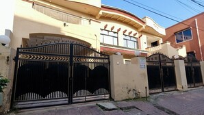 Ένα διώροφο κτίριο με περιφραγμένη είσοδο, μπαλκόνι και πινακίδα που υποδεικνύει την ύπαρξη συστήματος ασφαλείας.