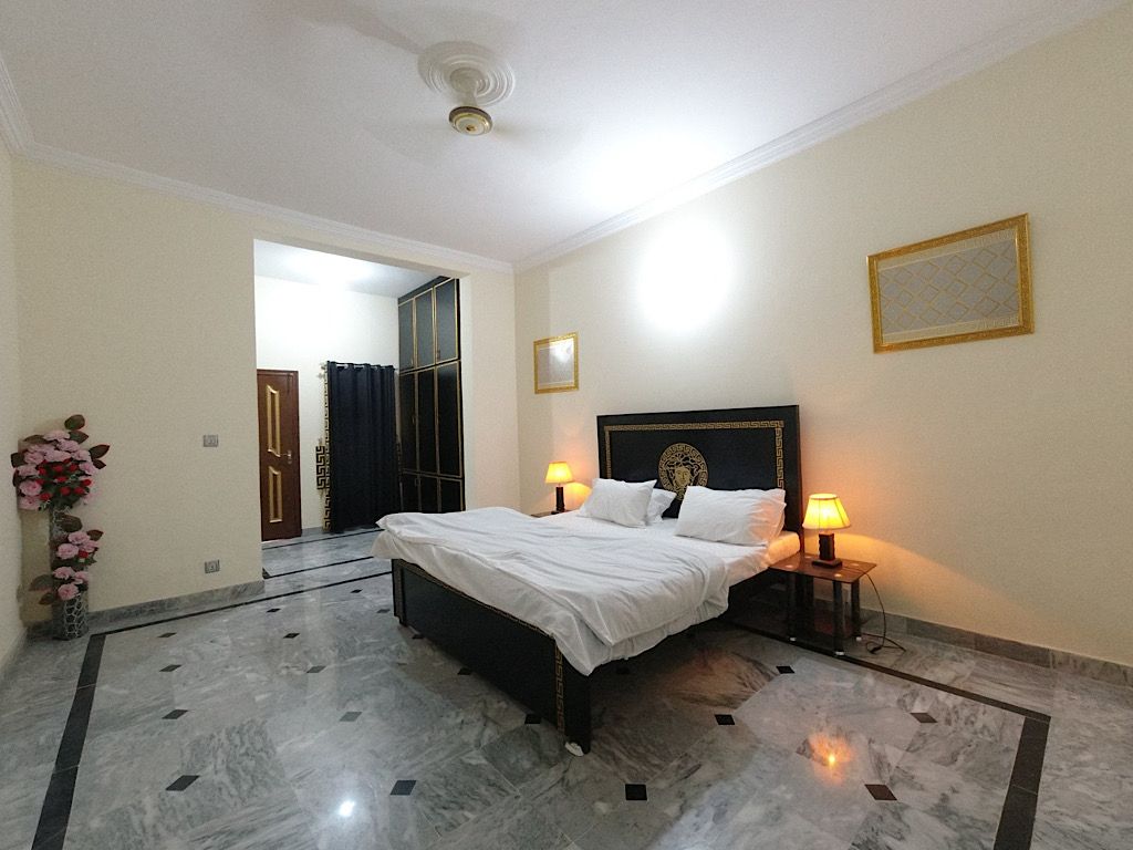 Une chambre d’hôtel avec un grand lit, deux tables de chevet avec des lampes, un vase de fleurs et une porte donnant sur une autre pièce.