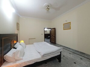 A hotel room with a bed, a headboard, a lamp, and a door leading to another room. - Room-serene Guest Room Retreat in Rawalp (Rawalpindi)