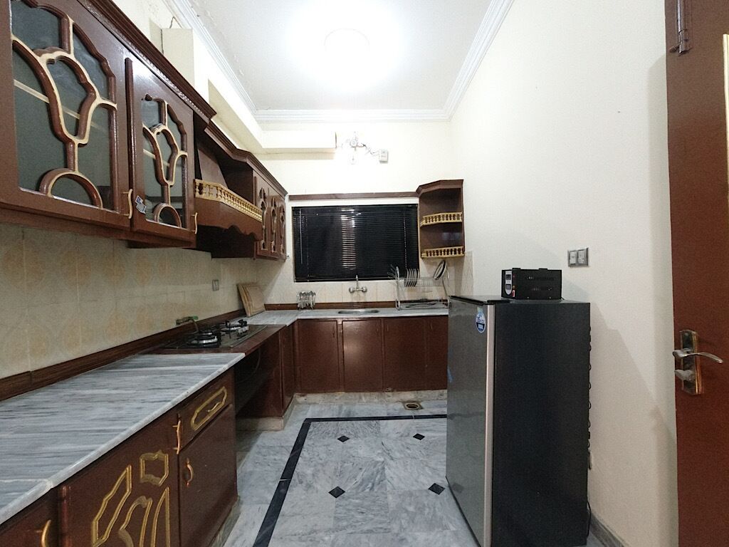 Una cocina compacta con armarios de madera oscura, encimera de mármol y refrigerador negro.