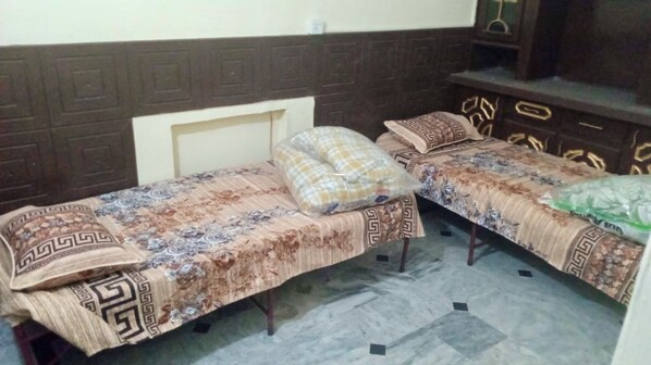 Two single beds with patterned bedspreads and matching pillows, a wooden headboard, and a tiled floor. - Room-room Serene Retreat in Rawalpindi - (Rawalpindi)