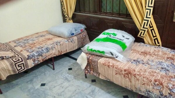 Two single beds with patterned bedspreads, a large pillow, and a bag of laundry on the floor. - Room-room Serene Retreat in Rawalpindi - (Rawalpindi)