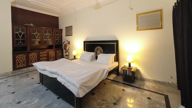 A hotel room with a large bed, two bedside lamps, a ceiling fan, and a decorative cabinet. - Room-room Serene Guest Room Retreat in R (Rawalpindi)