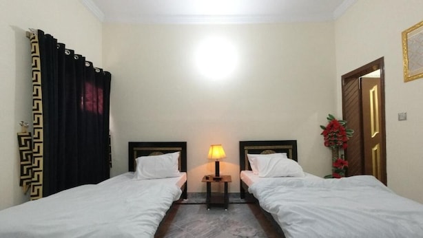 Une chambre d’hôtel avec deux lits simples, une table de chevet avec une lampe, un sol en marbre et une porte ornée d’un cadre décoratif.