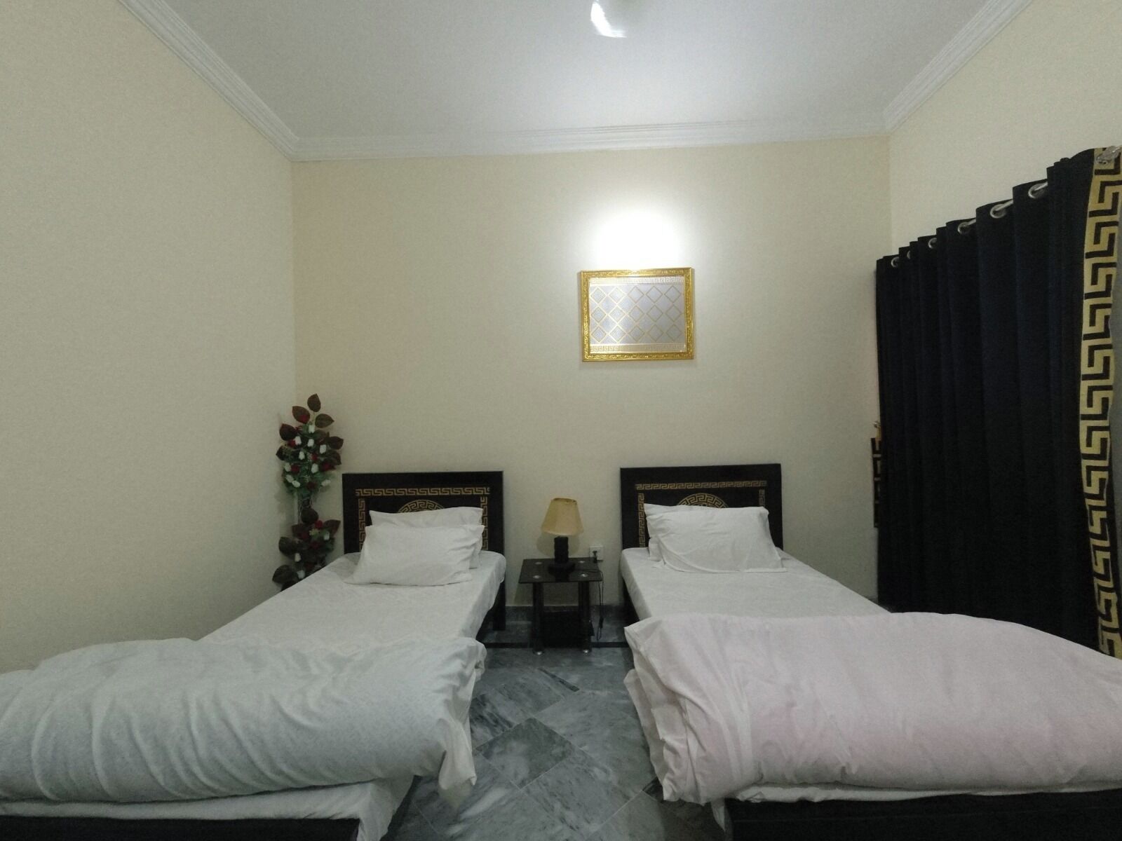 Habitación de hotel con dos camas individuales, una mesita con lámpara, un cuadro enmarcado en la pared y una cortina con estampado geométrico.