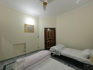 Ein Zimmer mit zwei Einzelbetten, einer Holztür und einem kleinen Fenster.
