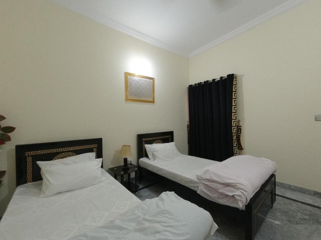 Ein Hotelzimmer mit zwei Einzelbetten, einem Nachttisch mit Lampe, einem gerahmten Bild an der Wand und einem Vorhang mit geometrischem Muster.