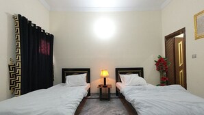A hotel room with two single beds, a nightstand with a lamp, a marble floor, and a door with a decorative frame. - Room-cozy Guest Room in Rawalpindi - Per (Rawalpindi)