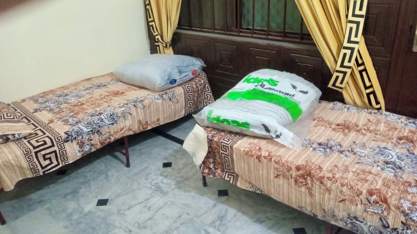 Quarto com duas camas de solteiro, cada uma com colcha estampada e um travesseiro. Há uma grande cesta de roupa suja na cama em primeiro plano.