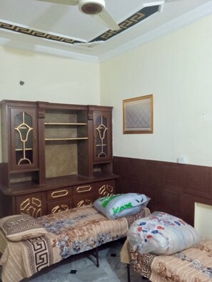 A bedroom with a wooden wardrobe, two beds with patterned bedding, and a ceiling fan. - Room-room Serene Retreat in Rawalpindi - (Rawalpindi)