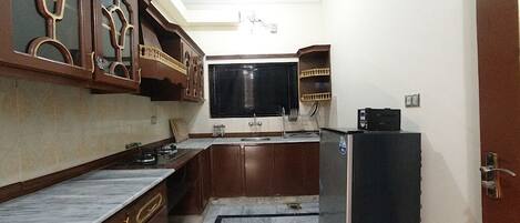 A compact kitchen with dark wooden cabinets, a marble countertop, and a black refrigerator.