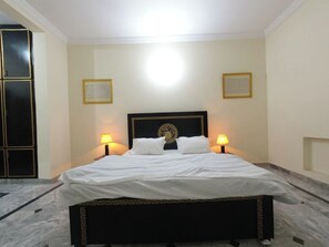 A hotel room with a bed, two bedside lamps, a decorative headboard, and a marble floor. - Room-room Serene Retreat in Rawalpindi - (Rawalpindi)