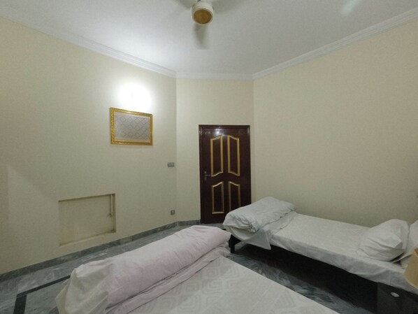 A small, clean room with two single beds, a wooden door, and a small window with a decorative frame.