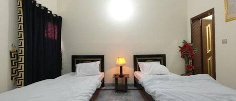 A hotel room with two single beds, a nightstand with a lamp, a marble floor, and a door with a decorative frame.