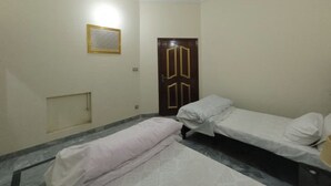 A room with two single beds, a wooden door, a small window with a decorative frame, and a ceiling fan.