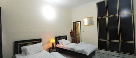 A hotel room with two beds, a ceiling fan, a nightstand with a lamp, a mirror, and a wardrobe.