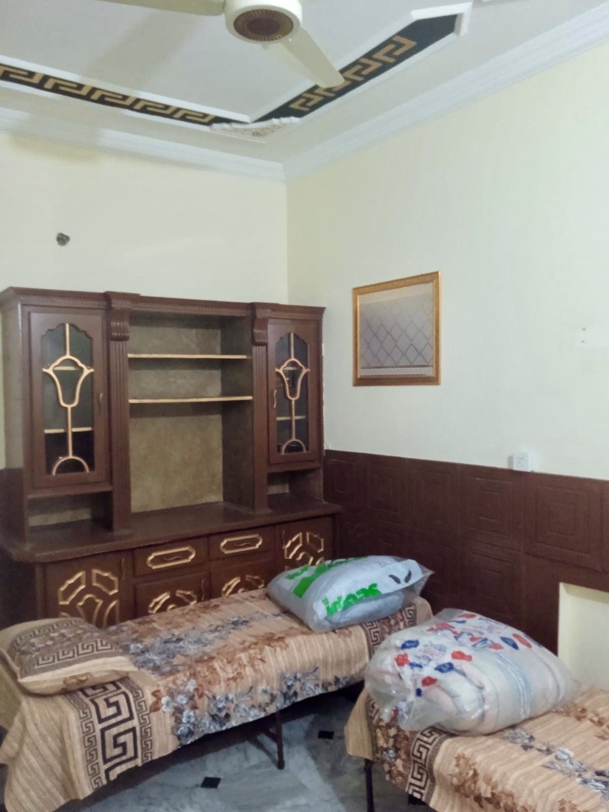 A bedroom with a wooden wardrobe, two beds with patterned bedding, and a ceiling fan.