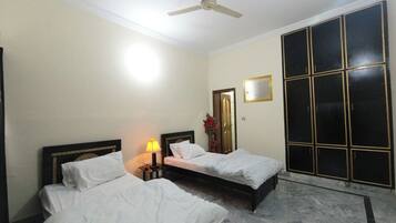 Une chambre d’hôtel avec deux lits, un ventilateur de plafond, une table de chevet avec une lampe, un miroir et une armoire.