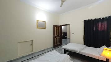 Une chambre d’hôtel avec deux lits simples, un ventilateur de plafond, un miroir, une porte et un rideau.