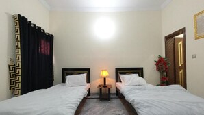 Camera d'albergo con due letti singoli, un comodino con una lampada, un pavimento in marmo e una porta con cornice decorativa.