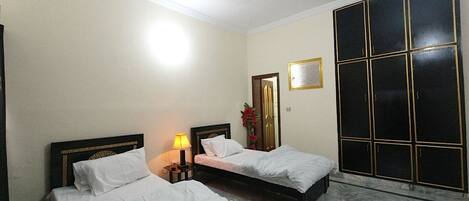 A hotel room with two beds, a ceiling fan, a nightstand with a lamp, a large window with a view, and a wardrobe.