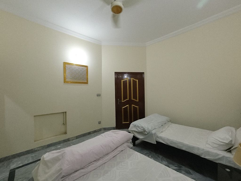 Een kamer met twee eenpersoonsbedden, een houten deur, een klein raam en een plafondventilator.