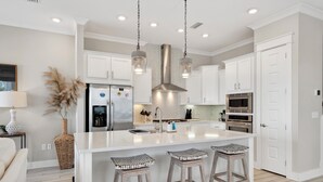 A modern kitchen with white cabinetry, a large island with stools, stainless steel appliances, and pendant lighting.